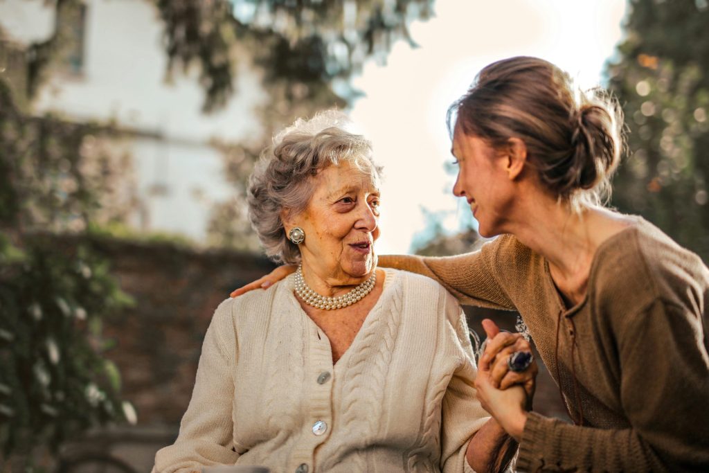 Une femme âgée et sa fille adulte partagent un moment joyeux et affectueux dans un jardin ensoleillé.